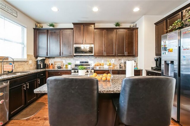 kitchen featuring appliances with stainless steel finishes, a sink, a center island, light stone counters, and dark brown cabinetry