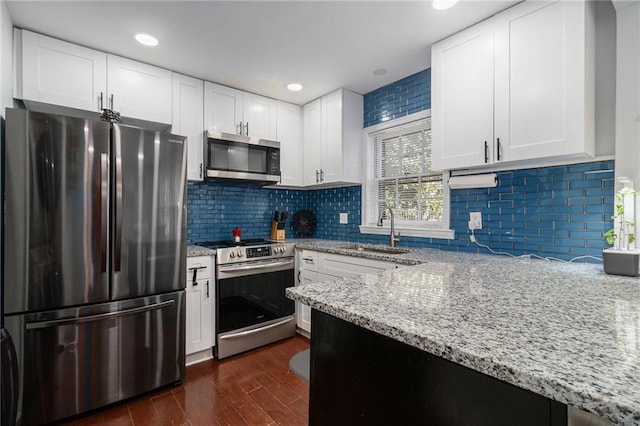 kitchen with a sink, light stone countertops, dark wood-type flooring, and appliances with stainless steel finishes