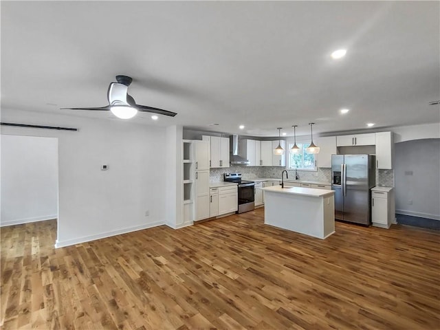 kitchen featuring a center island with sink, a sink, stainless steel appliances, light countertops, and wall chimney exhaust hood