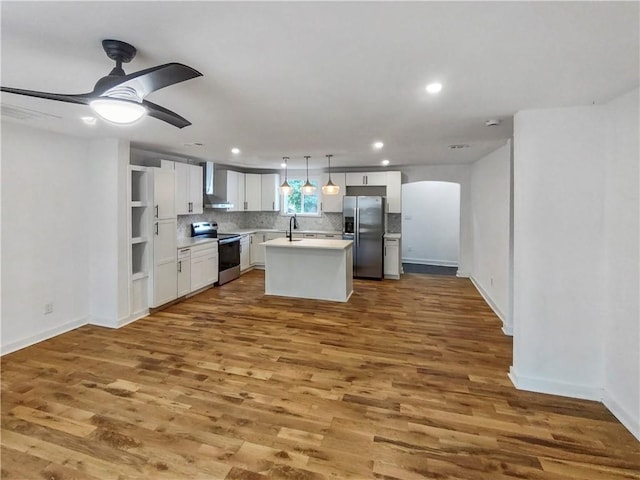 kitchen with tasteful backsplash, dark wood finished floors, appliances with stainless steel finishes, white cabinets, and wall chimney range hood