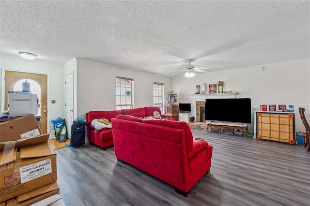 living room with a ceiling fan, a brick fireplace, wood finished floors, and a textured ceiling