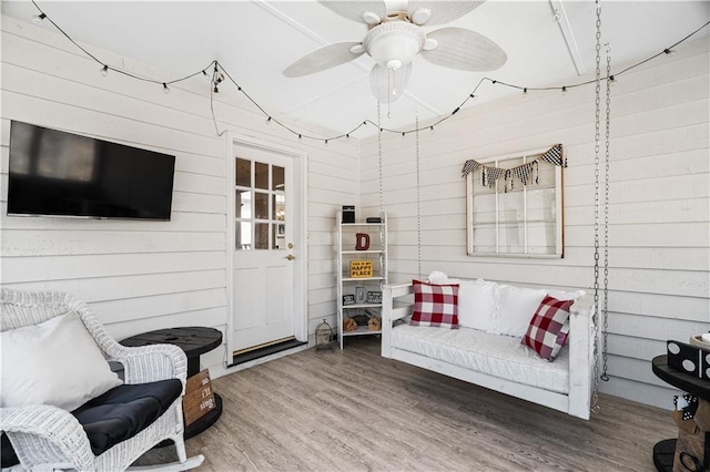 sitting room with ceiling fan, wooden walls, and hardwood / wood-style flooring