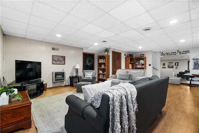 living room with a drop ceiling, hardwood / wood-style flooring, and heating unit