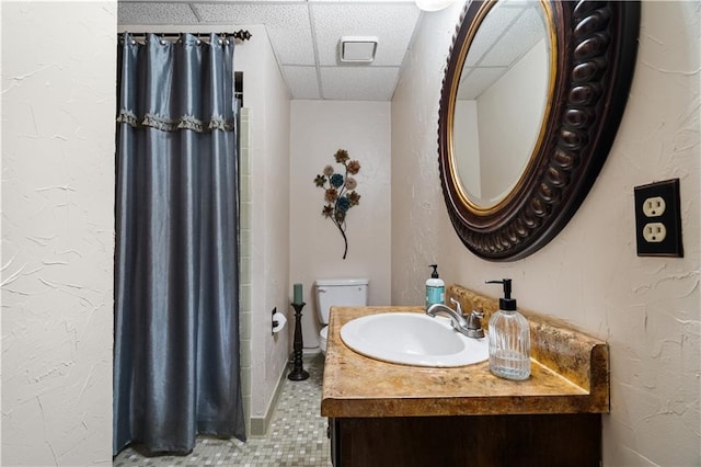 bathroom featuring tile patterned floors, vanity, toilet, and a drop ceiling