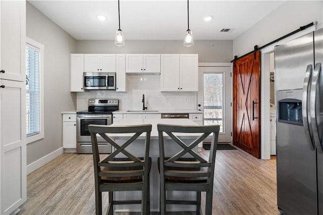 kitchen with sink, a barn door, decorative light fixtures, white cabinetry, and stainless steel appliances