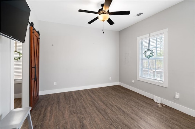 unfurnished room featuring ceiling fan, a barn door, and dark hardwood / wood-style flooring