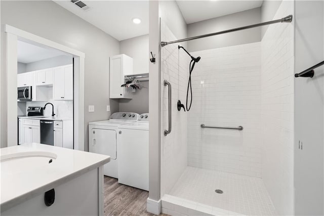 bathroom with hardwood / wood-style flooring, vanity, washing machine and dryer, and a tile shower