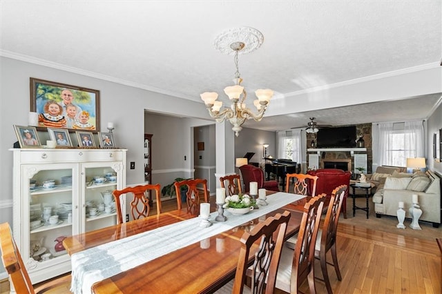 dining space featuring crown molding, light hardwood / wood-style floors, a textured ceiling, a fireplace, and ceiling fan with notable chandelier