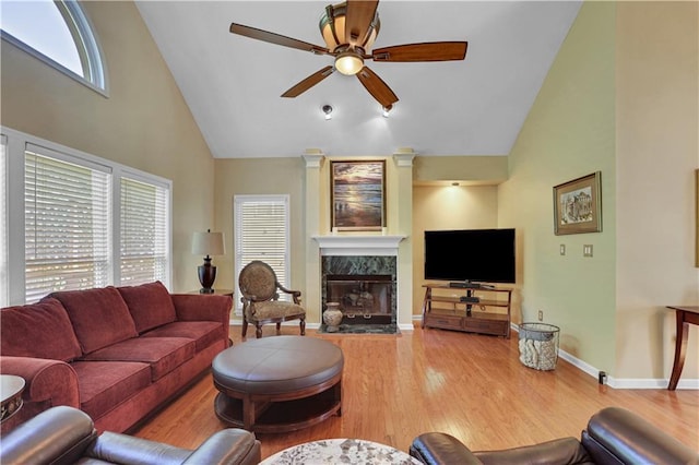 living room featuring a high end fireplace, high vaulted ceiling, light hardwood / wood-style floors, and ceiling fan