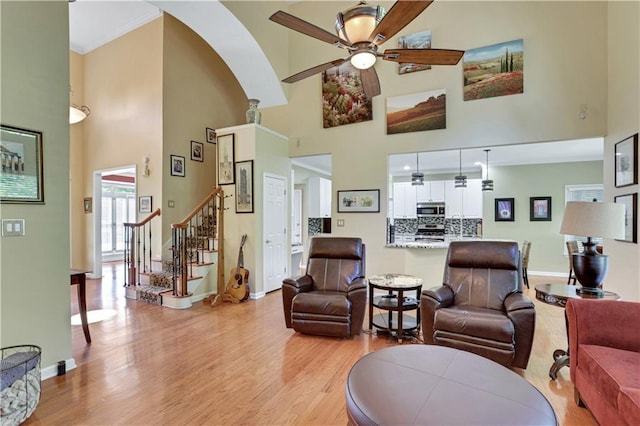 living room with a high ceiling, ceiling fan, and light wood-type flooring