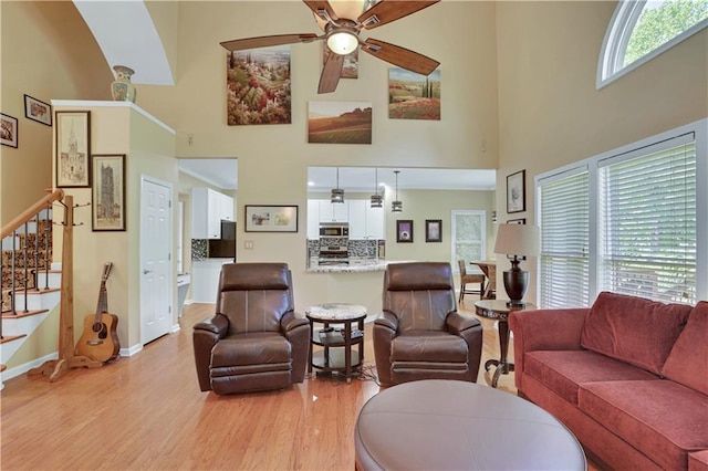 living room featuring a towering ceiling, ceiling fan, and light wood-type flooring