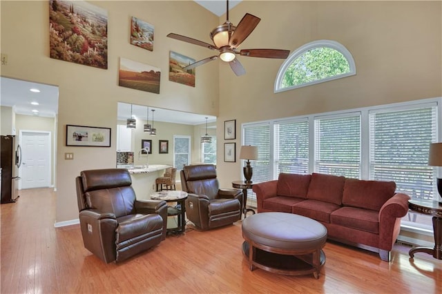 living room featuring ceiling fan, a towering ceiling, and light hardwood / wood-style floors