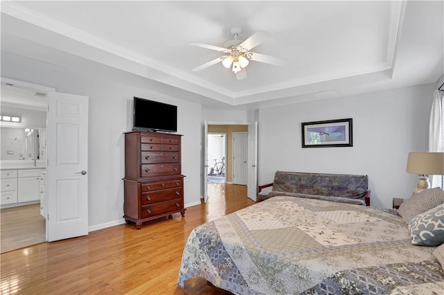 bedroom with connected bathroom, ceiling fan, a tray ceiling, and light hardwood / wood-style flooring