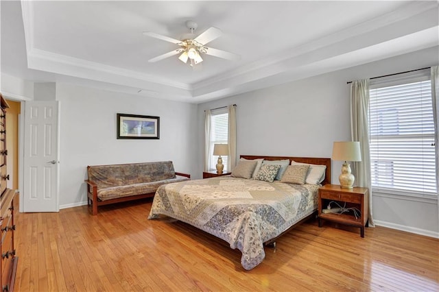 bedroom featuring multiple windows, light wood-type flooring, ceiling fan, and a raised ceiling