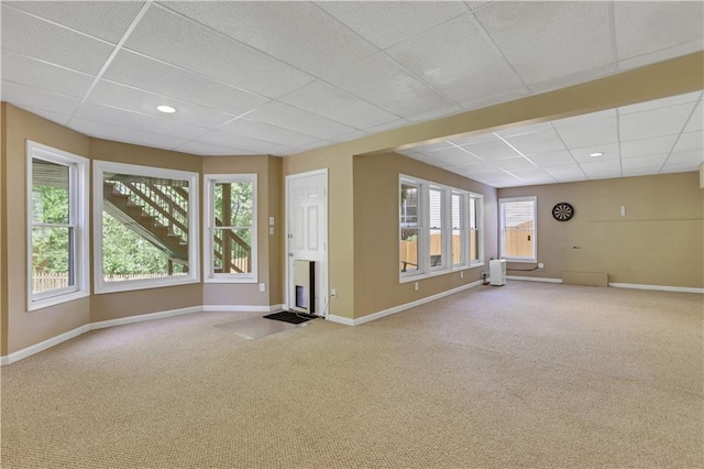 empty room with a paneled ceiling, light carpet, a fireplace, and a healthy amount of sunlight