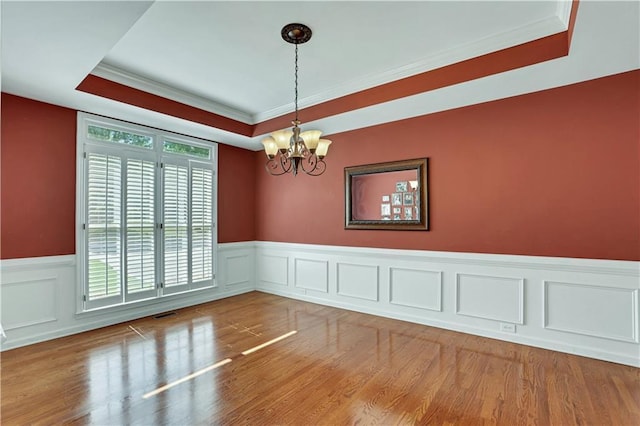 unfurnished room featuring a raised ceiling, plenty of natural light, a notable chandelier, and light hardwood / wood-style flooring