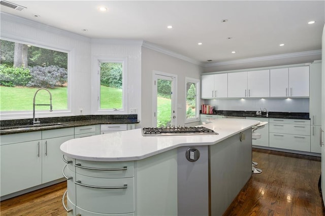 kitchen featuring visible vents, a kitchen island, dark wood-style flooring, a sink, and stainless steel gas stovetop