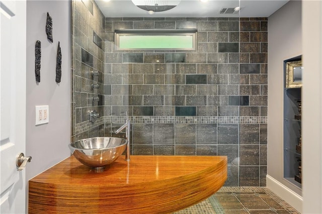 bathroom with visible vents, a tile shower, and a sink