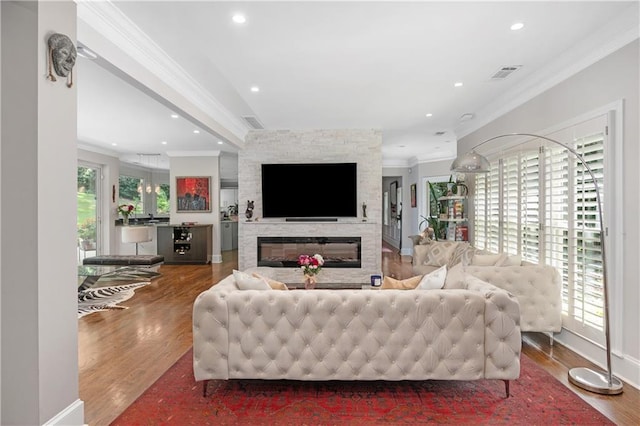 living room featuring a stone fireplace, recessed lighting, wood finished floors, and ornamental molding