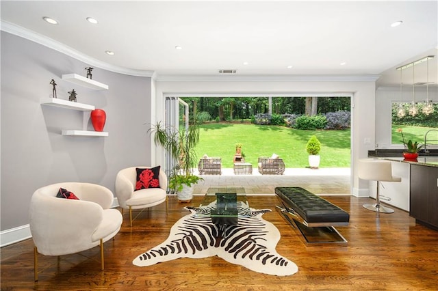 living area with wood finished floors, visible vents, baseboards, recessed lighting, and crown molding