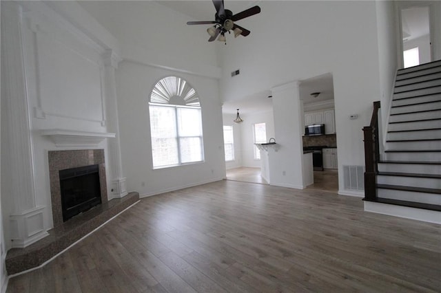 unfurnished living room featuring ceiling fan, a tile fireplace, wood finished floors, visible vents, and stairs