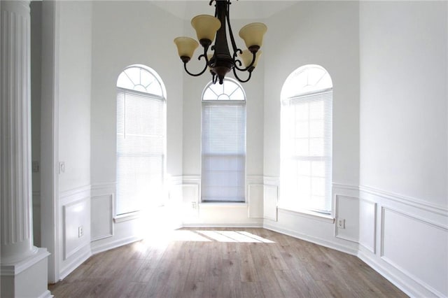 unfurnished dining area with ornate columns, a notable chandelier, and light wood-type flooring