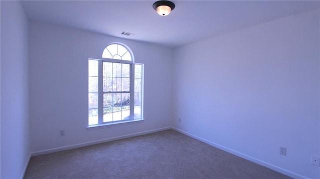 spare room featuring dark colored carpet, visible vents, and baseboards