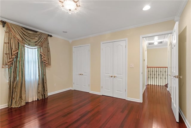 unfurnished bedroom featuring multiple closets, crown molding, and dark hardwood / wood-style floors