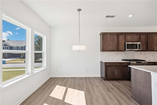 kitchen with backsplash, dark brown cabinets, stainless steel appliances, and hanging light fixtures