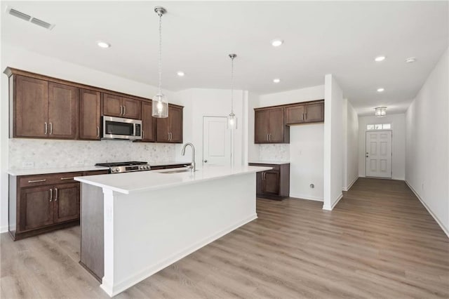 kitchen featuring sink, hanging light fixtures, backsplash, an island with sink, and range