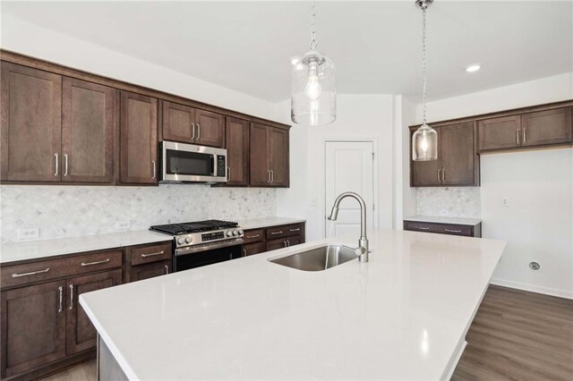 kitchen with decorative light fixtures, sink, stainless steel appliances, and a center island with sink