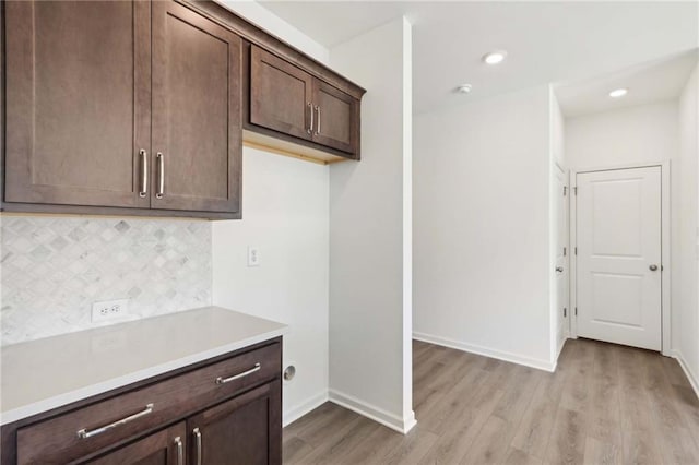 kitchen with dark brown cabinets, light wood-type flooring, and tasteful backsplash