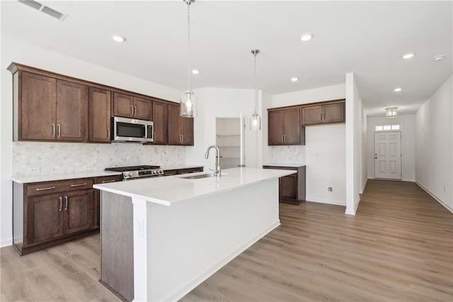 kitchen with stove, a kitchen island with sink, sink, hanging light fixtures, and light wood-type flooring