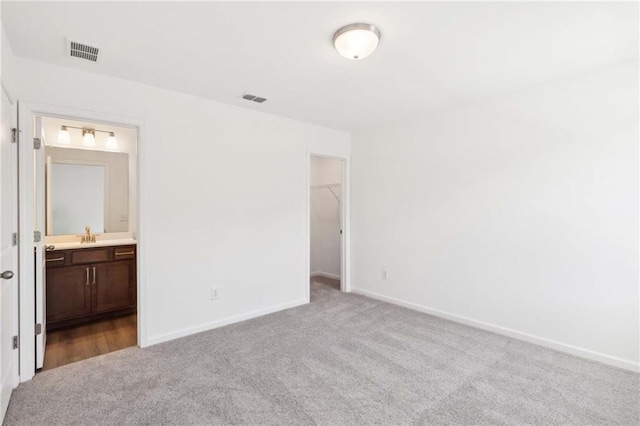 unfurnished bedroom featuring a walk in closet, ensuite bath, light colored carpet, sink, and a closet