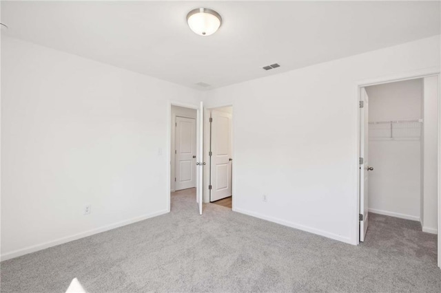 unfurnished bedroom with a spacious closet, light carpet, and a closet