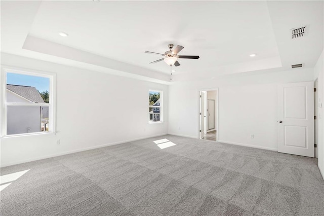 carpeted spare room featuring ceiling fan, a healthy amount of sunlight, and a tray ceiling