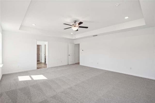 empty room featuring a tray ceiling, ceiling fan, and carpet floors