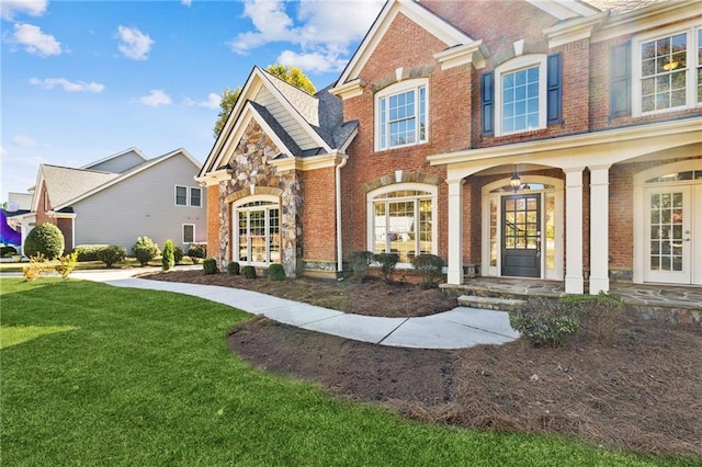 view of front of home featuring stone siding, brick siding, a front lawn, and french doors