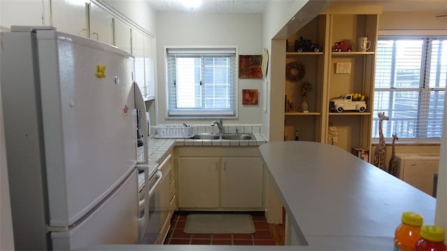 kitchen with sink, fridge, tile counters, dark tile patterned flooring, and cream cabinets