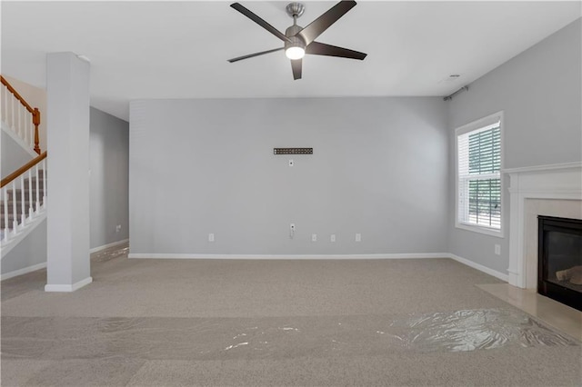 unfurnished living room featuring ceiling fan, light colored carpet, and a high end fireplace