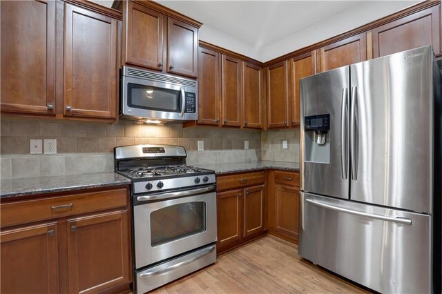 kitchen with dark stone counters, decorative backsplash, appliances with stainless steel finishes, and light hardwood / wood-style flooring