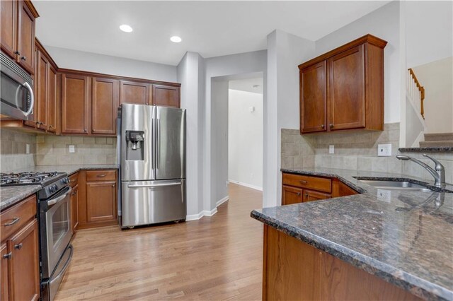 kitchen with appliances with stainless steel finishes, light wood-type flooring, backsplash, and sink