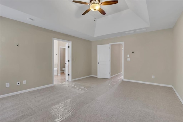 empty room featuring light carpet, a raised ceiling, and ceiling fan