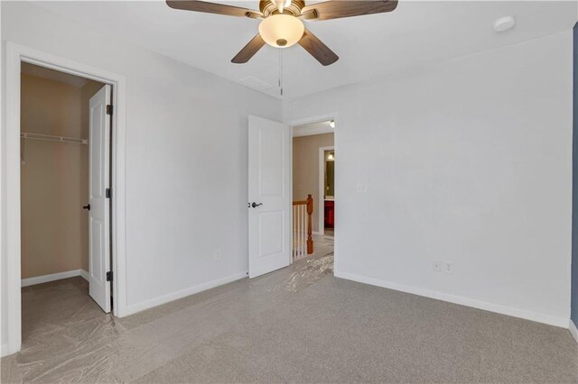 unfurnished bedroom with a walk in closet, ceiling fan, a closet, and light colored carpet