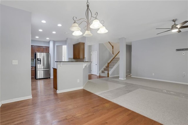 kitchen featuring stainless steel fridge with ice dispenser, kitchen peninsula, pendant lighting, wood-type flooring, and ceiling fan with notable chandelier