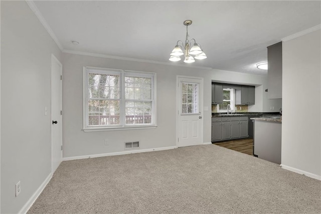 unfurnished dining area with ornamental molding, sink, a notable chandelier, and dark carpet