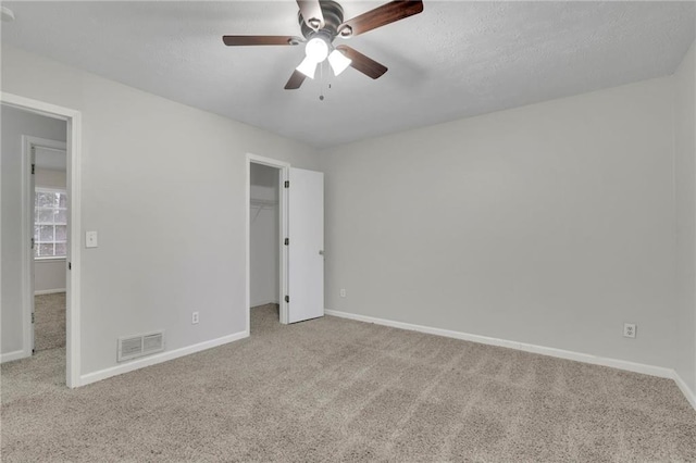 unfurnished bedroom featuring ceiling fan, light colored carpet, a spacious closet, and a closet