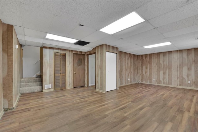 basement featuring hardwood / wood-style flooring, a paneled ceiling, and wood walls