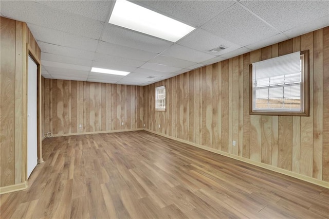 empty room with plenty of natural light, wooden walls, light hardwood / wood-style flooring, and a drop ceiling