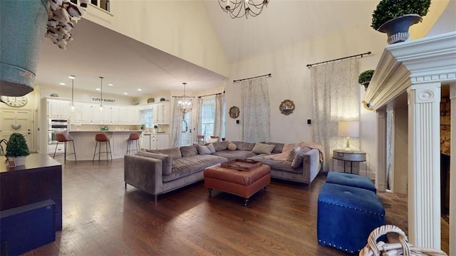 living room featuring hardwood / wood-style flooring, ornate columns, high vaulted ceiling, and an inviting chandelier